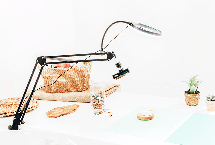 Mobile light arm hovering over a white table with flatly photography props, including small plant pots and teal paper.