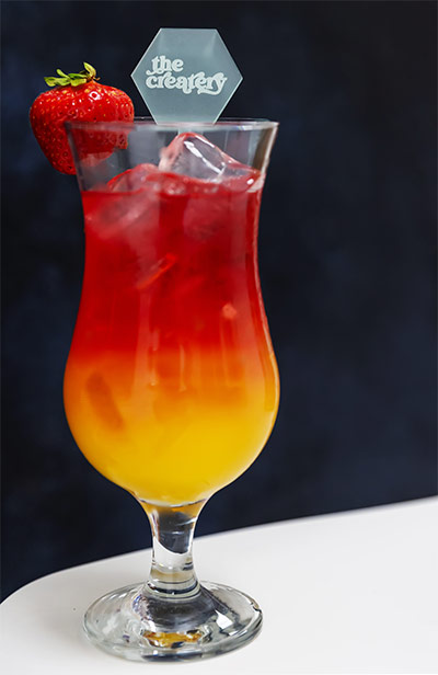 Red and yellow Createry cocktail with branded stirrer.