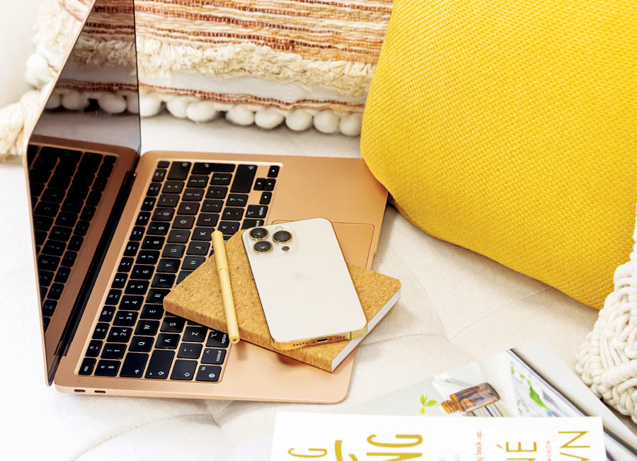 Laptop on sofa with phone, notebook and cushion.