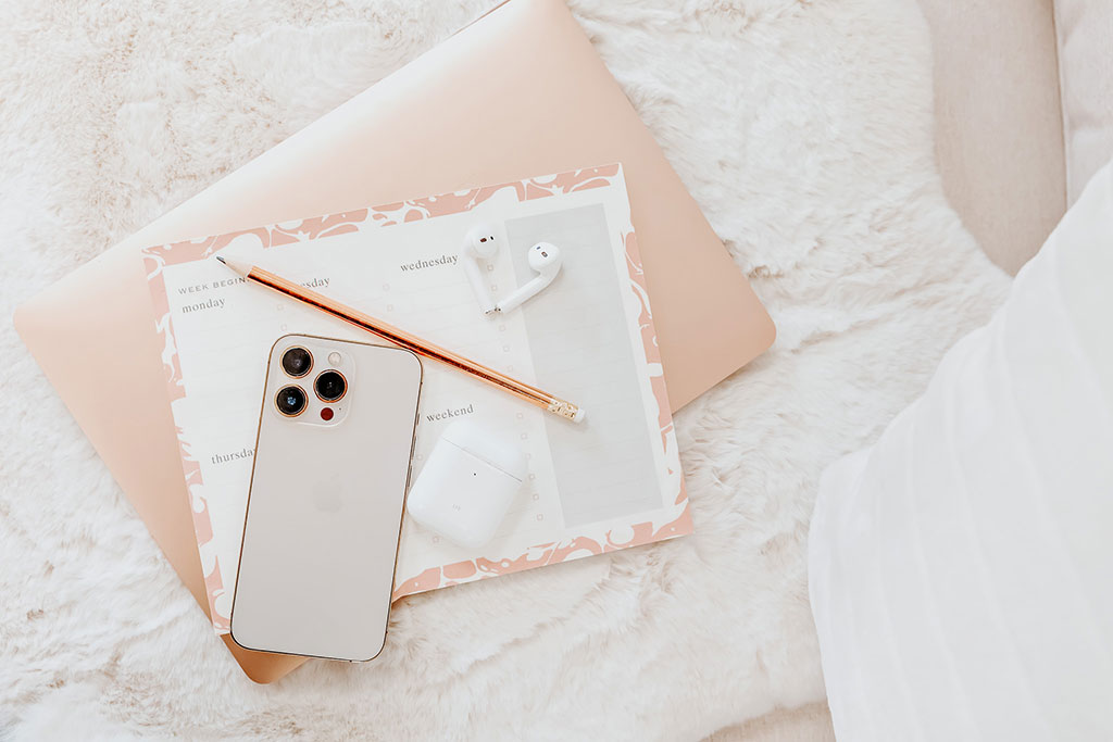 Phone, pencil, weekly planner on pink laptop on white faux fur throw.