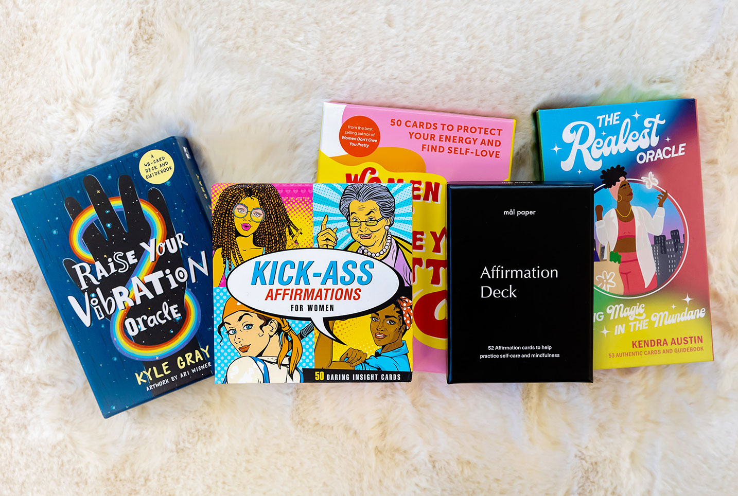 Decks of colourful affirmation and oracle cards spread out over a white fluffy rug.