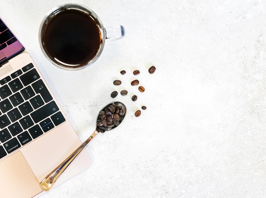 Laptop, coffee and spoon on white textured background.