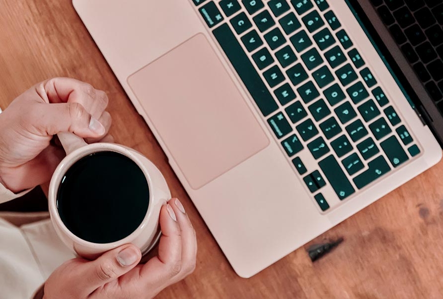 Woman sitting at laptop holding a cup of coffee - overhead view