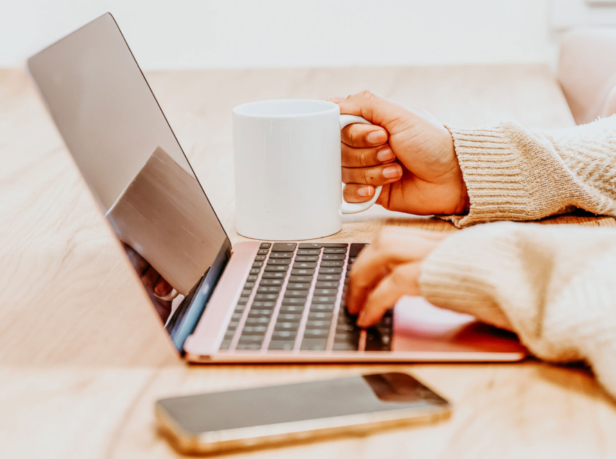 Woman holding coffee mug while typing on laptop