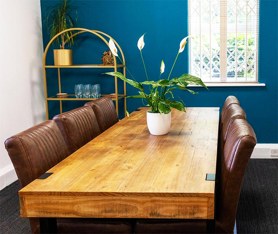 Meeting room wooden table with vegetarian leather chairs and teal wall.