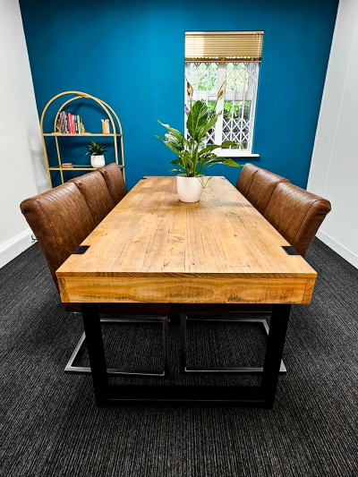 Wooden table with six brown faux leather chairs. Grey stripy carpet, teal feature wall and gold blind.