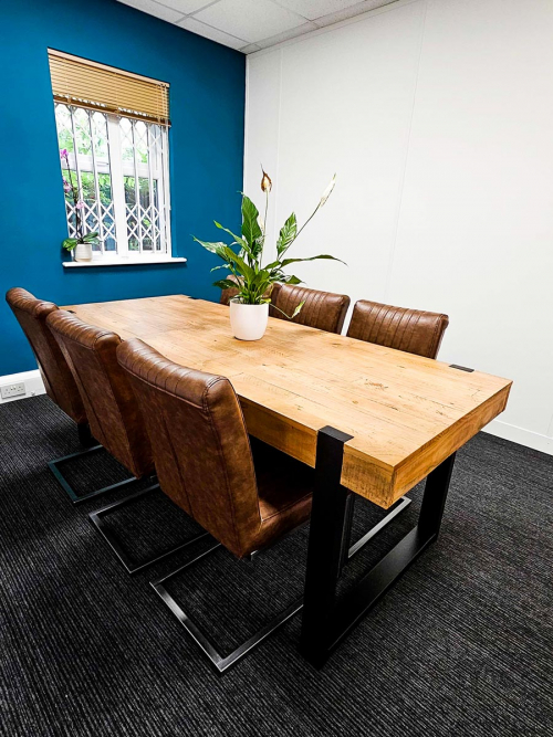 Angled view of the back of faux leather chairs, wooden table with lily, and teal feature wall with gold blind.